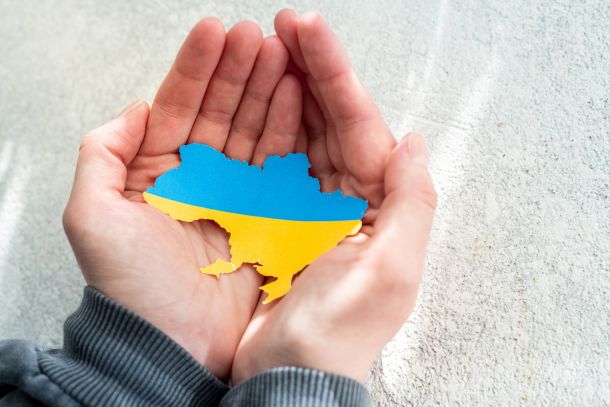 Hands holding national flag of Ukraine in the shape of the borders of Ukraine. Support for Ukraine